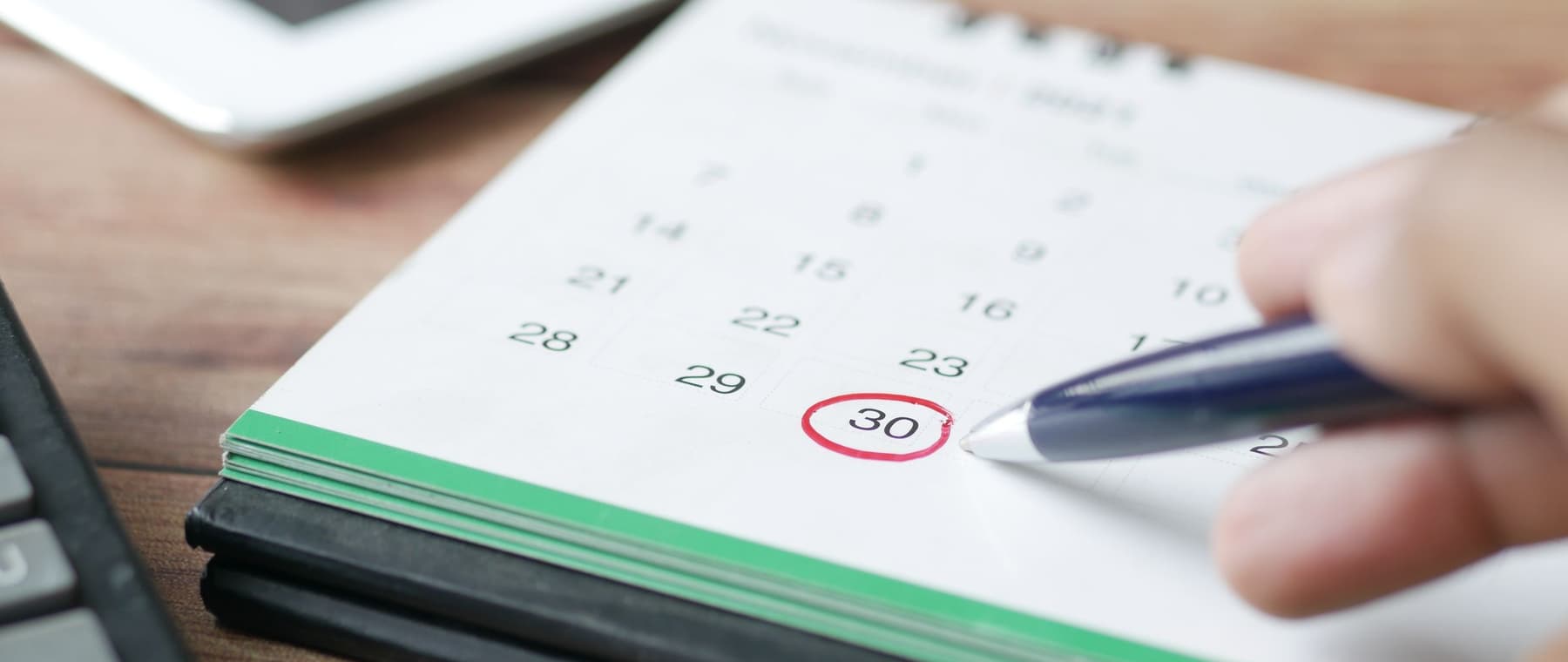 Een hand wijst met een pen een datum aan op een kalender
